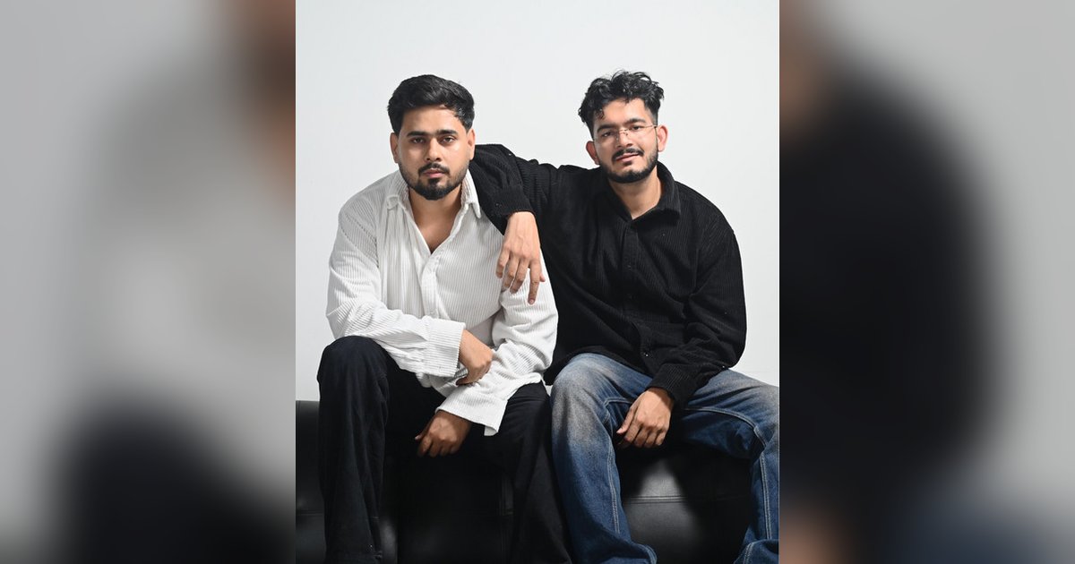Sumit and Anuj of Banjaare seated on a black sofa, one in a white shirt and one in black with his arm on the other's shoulder