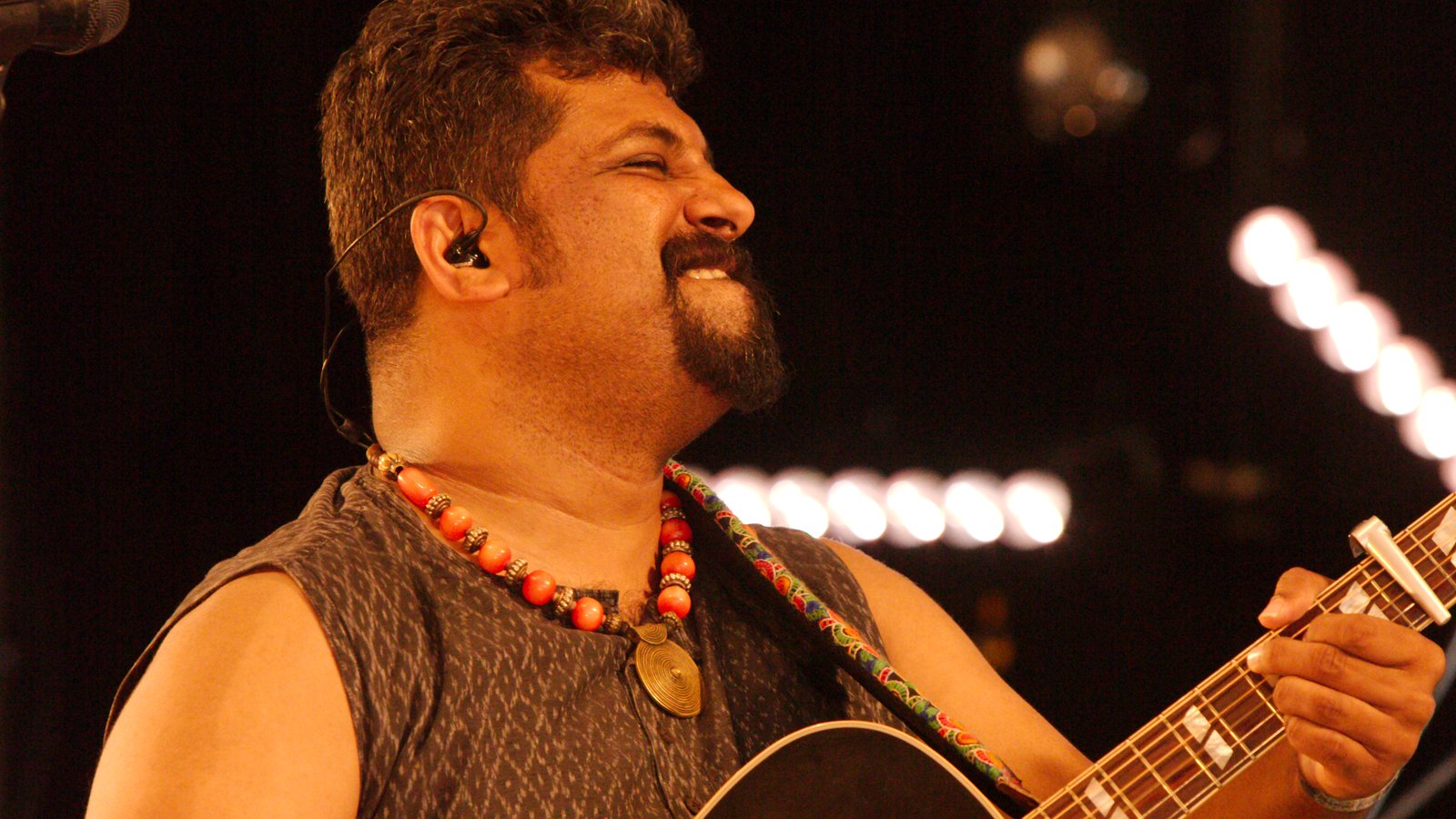 Raghu Dixit singing into a microphone on stage at Shrewsbury Folk Festival 2016