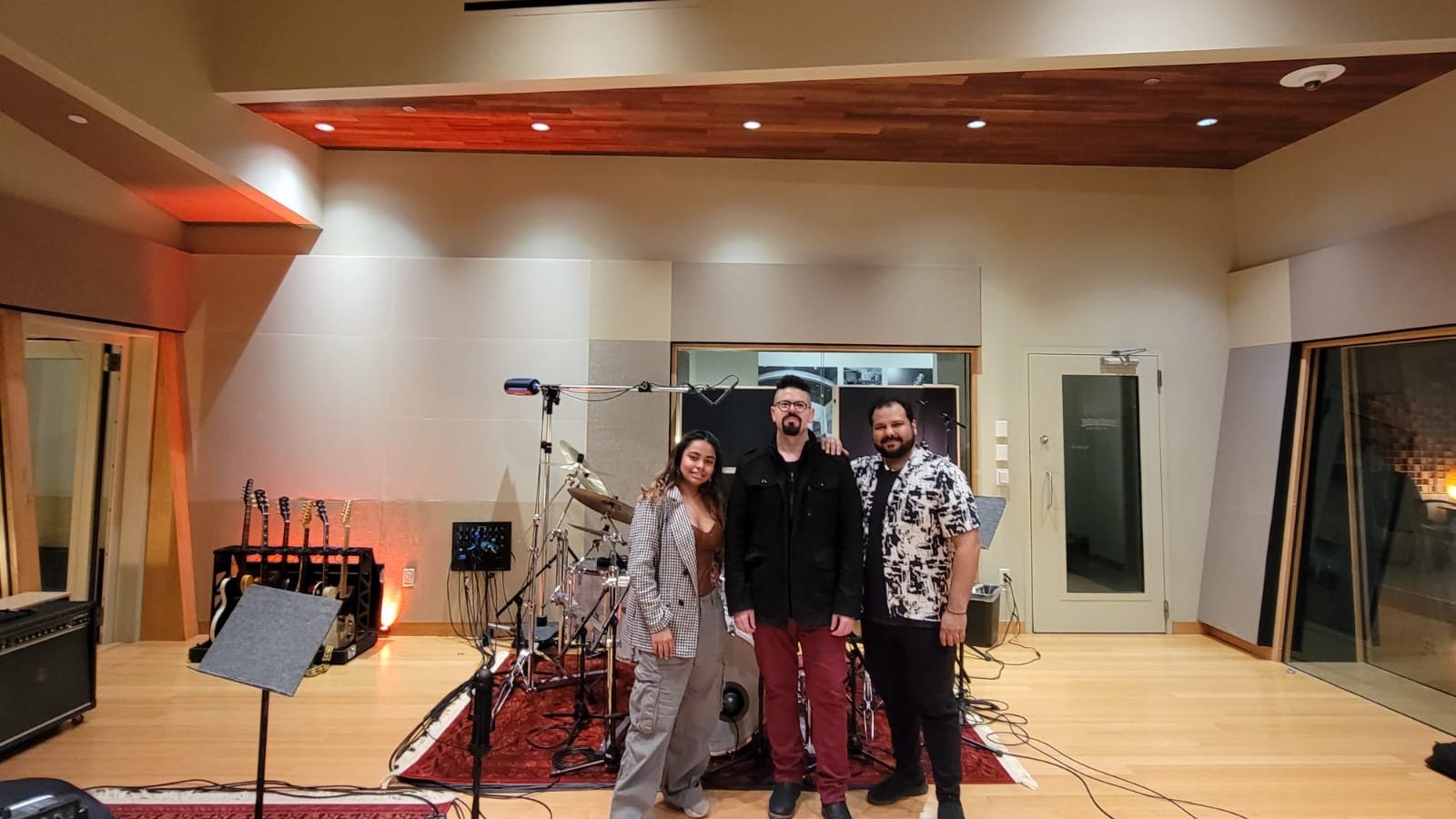 Bassist Mohini Dey, guitarist Jan Rivera and drummer Gino Banks standing together in a recording studio with drums and guitars behind them