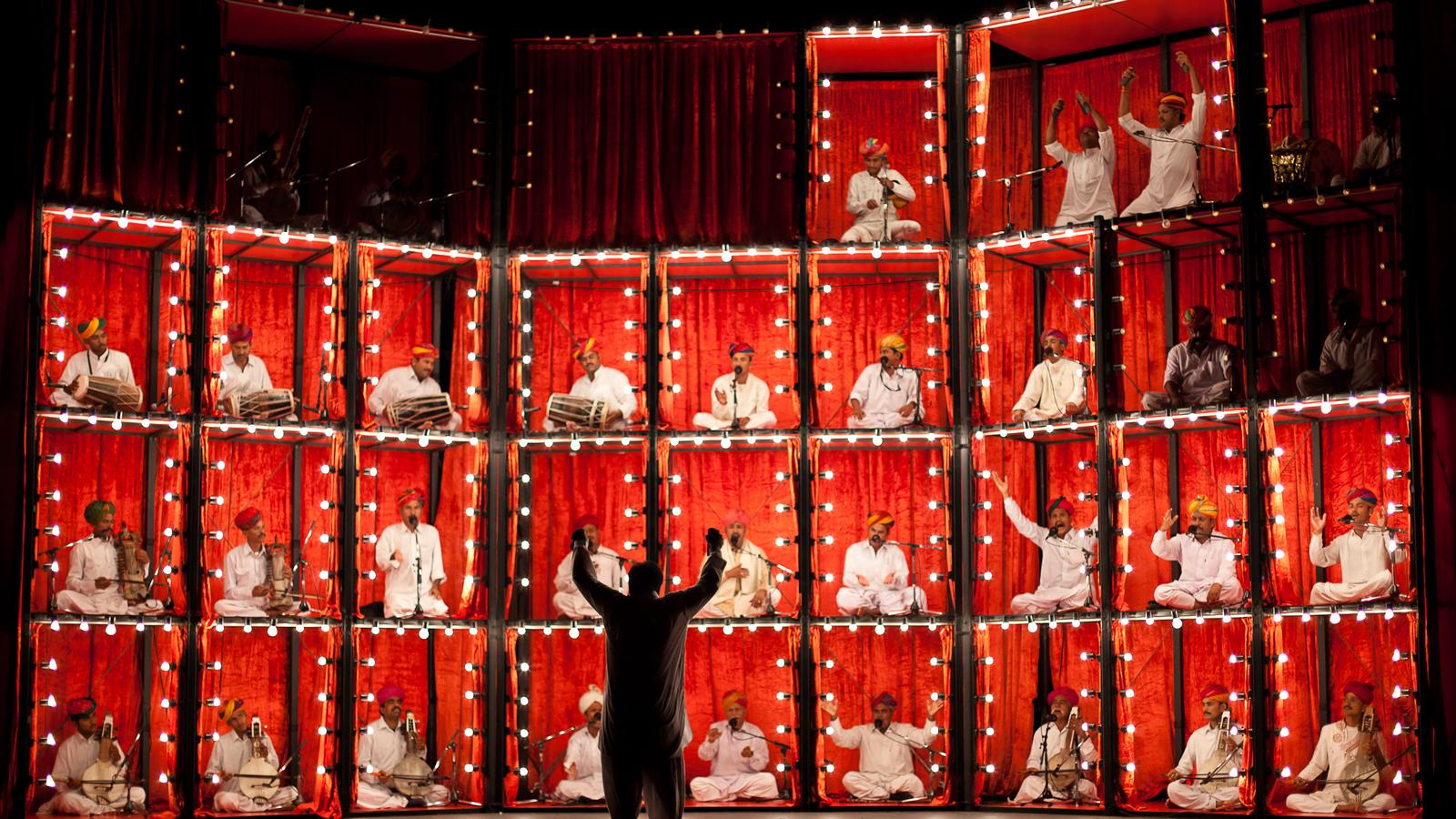 Dozens of Manganiyar musicians seated in lit, stacked red-curtained boxes during The Manganiyar Seduction at the 2011 Melbourne Festival