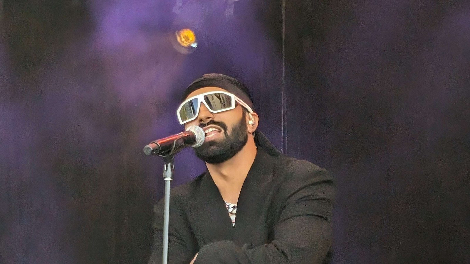 Prabh Deep in white sunglasses, a black headwrap and a black suit singing into a microphone on stage at SXSW Sydney 2024