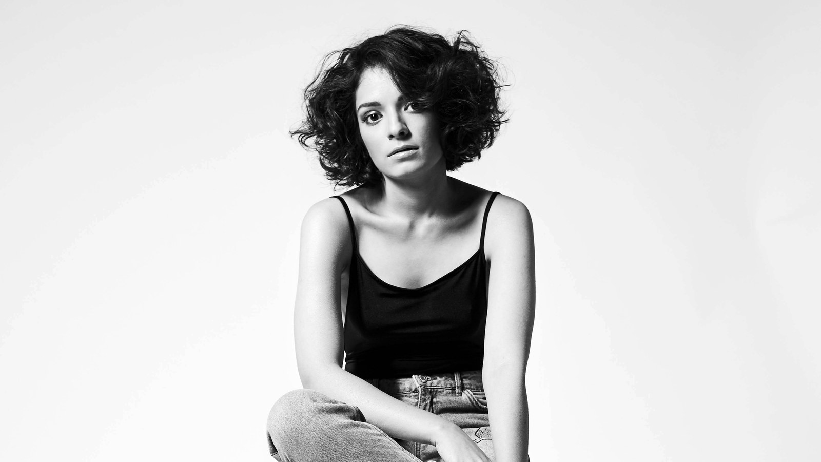 Black-and-white studio portrait of singer-songwriter Mali, seated against a plain white background