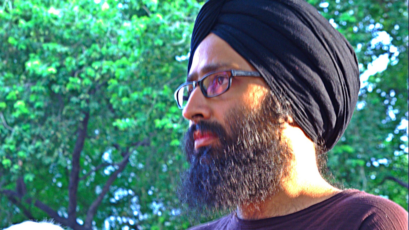Sufi rock singer Rabbi Shergill in a black turban and glasses, photographed in profile against green trees