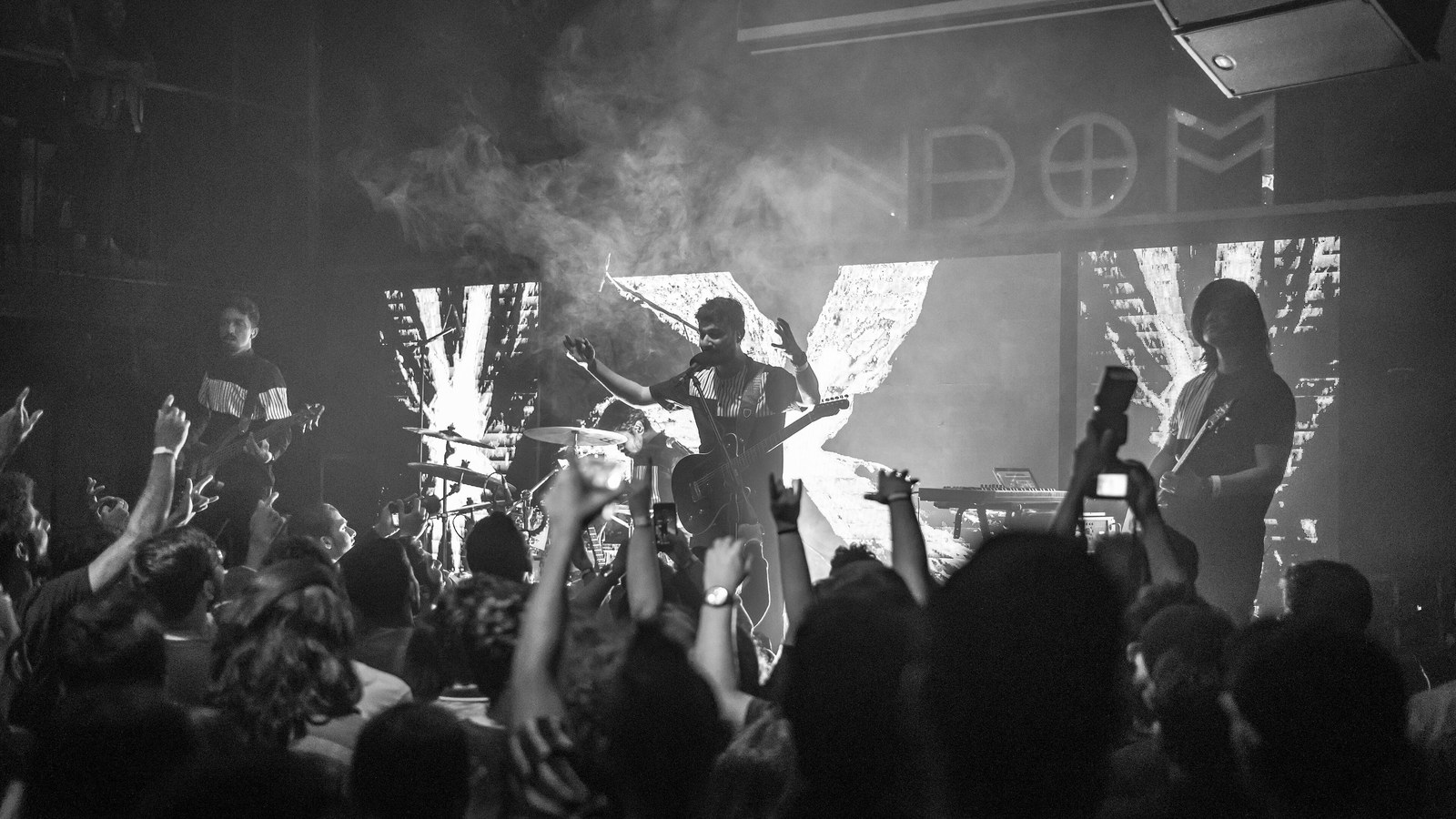 Post-rock band Aswekeepsearching performing to a crowd with raised hands in a smoky black-and-white concert shot in Bangalore
