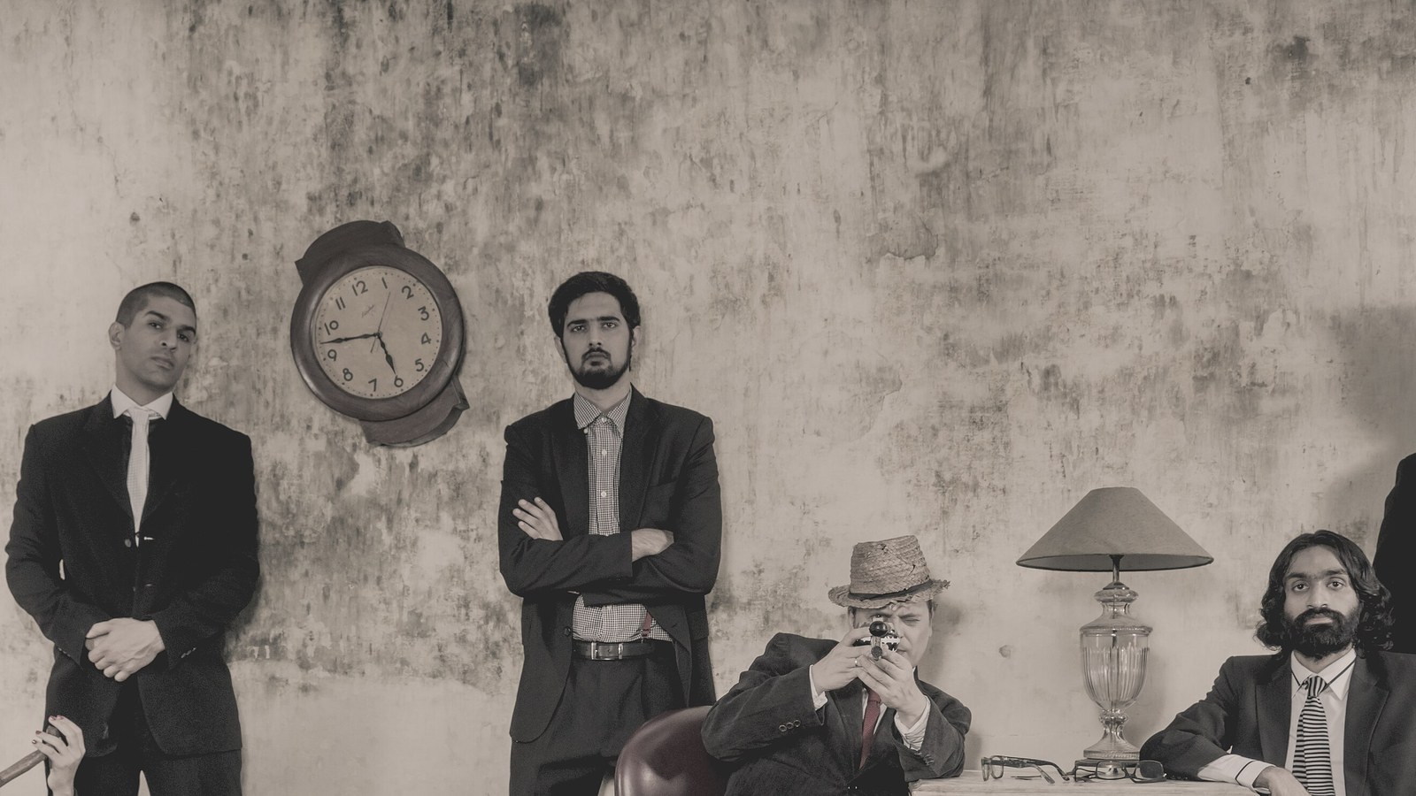 The Ska Vengers posing in suits against a weathered wall with a clock and table lamp in a sepia band photo