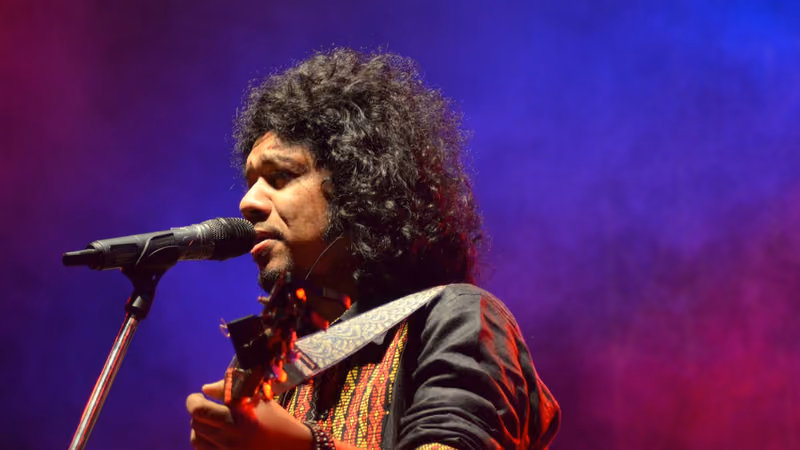 Papon singing into a microphone with a guitar under purple stage lights at Euphuism 2014